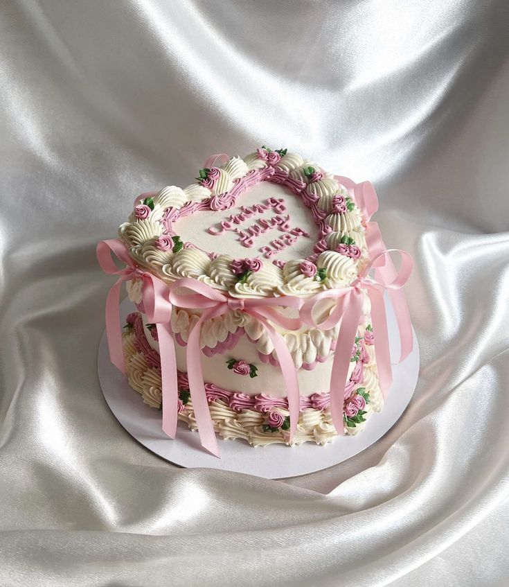 a heart shaped cake decorated with flowers and ribbons on a white tableclothed surface