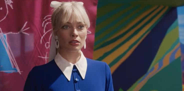 a woman with blonde hair wearing a blue shirt and white collared top standing in front of colorful backdrop