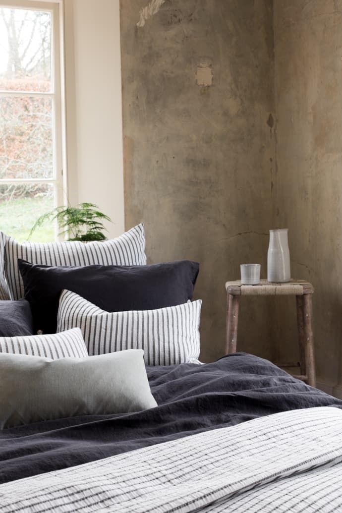 a bed with black and white striped pillows in front of a window, next to a small table