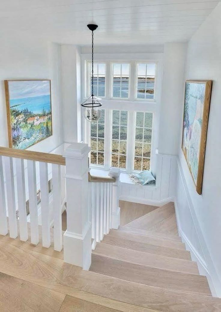 the stairs in this house are white and have wood treading on them, while paintings hang on the wall