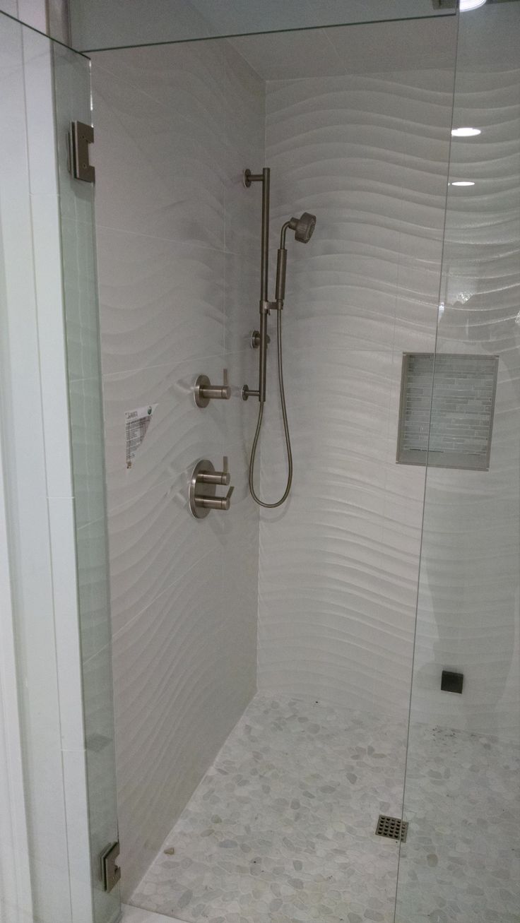 a walk in shower sitting next to a white tiled wall and floor with glass doors