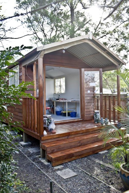 a small wooden cabin in the middle of some trees and bushes, with its door open