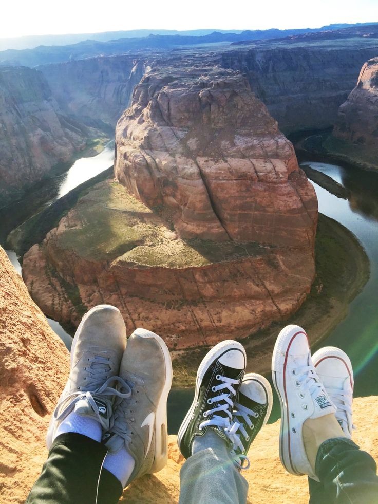 two people with their feet on the edge of a cliff overlooking a river and canyon