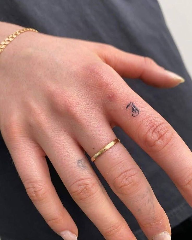 a woman's hand with a small tattoo on the middle finger and a gold ring