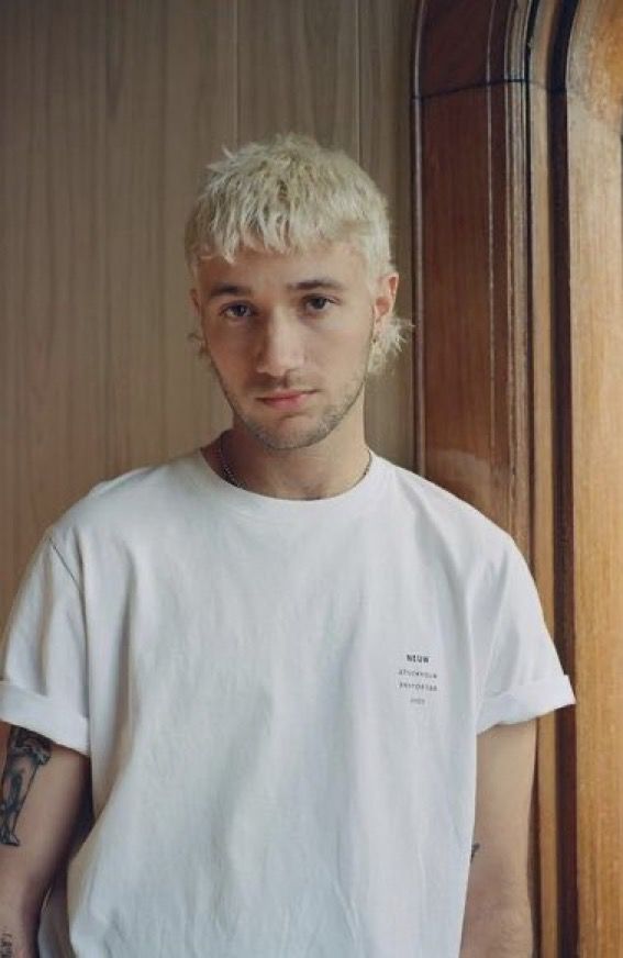 a man with blonde hair and tattoos standing in front of a wooden door