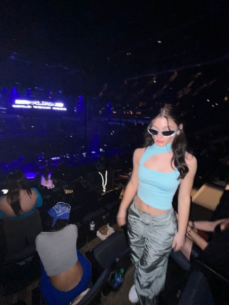 a woman standing in the middle of a crowd at a concert wearing sunglasses and a crop top