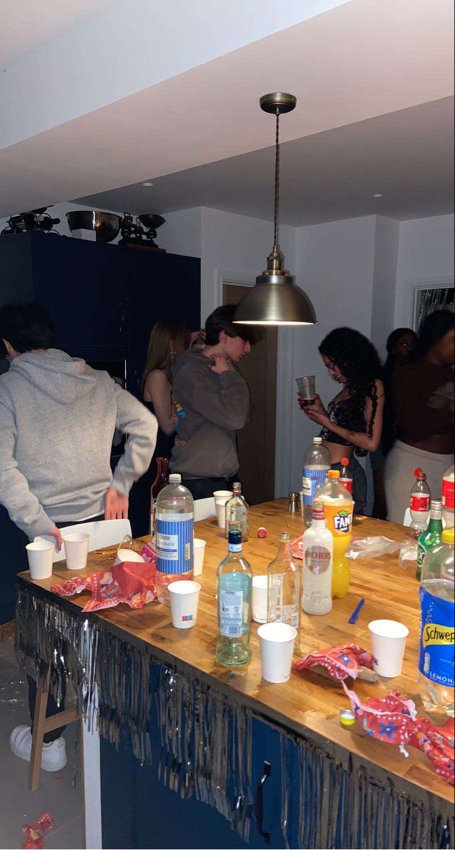 a group of people standing around a kitchen counter covered in condiments and drinks