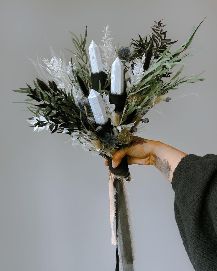 a person holding a bunch of flowers with candles in the middle and greenery on top