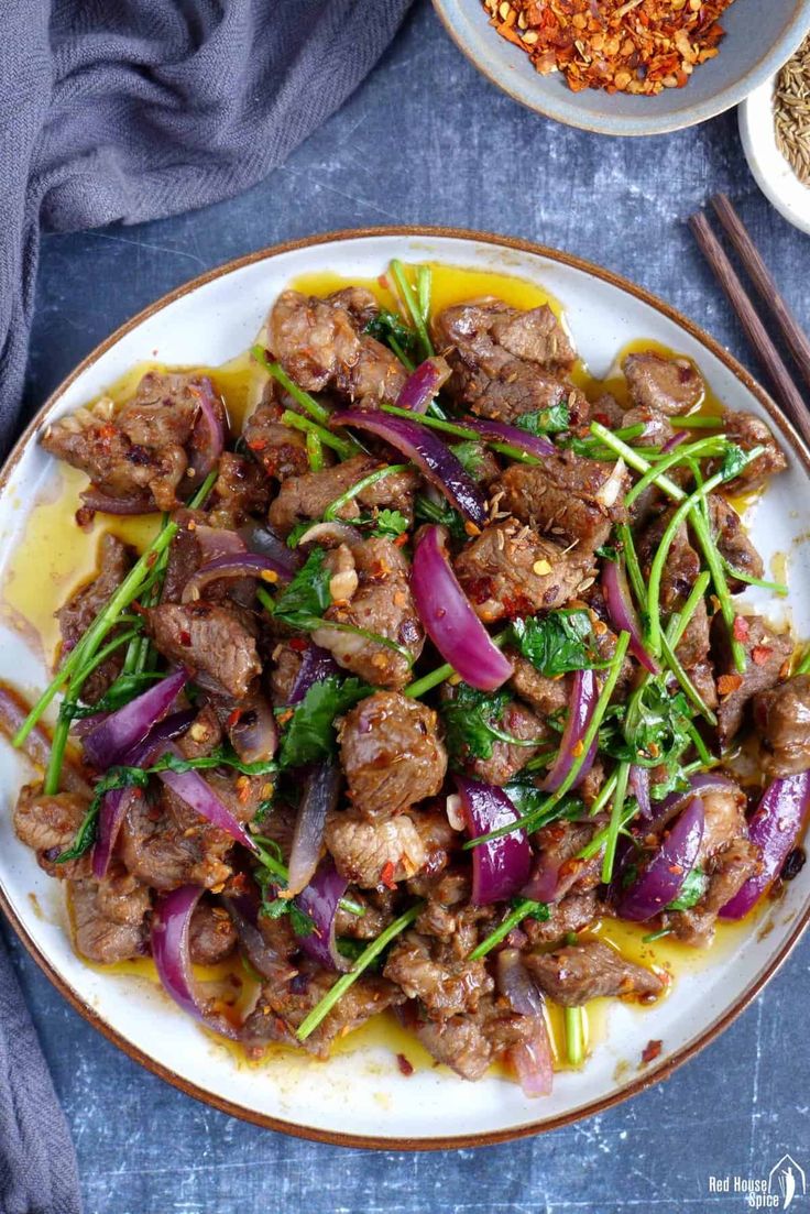 a white plate topped with meat and veggies next to bowls of seasoning