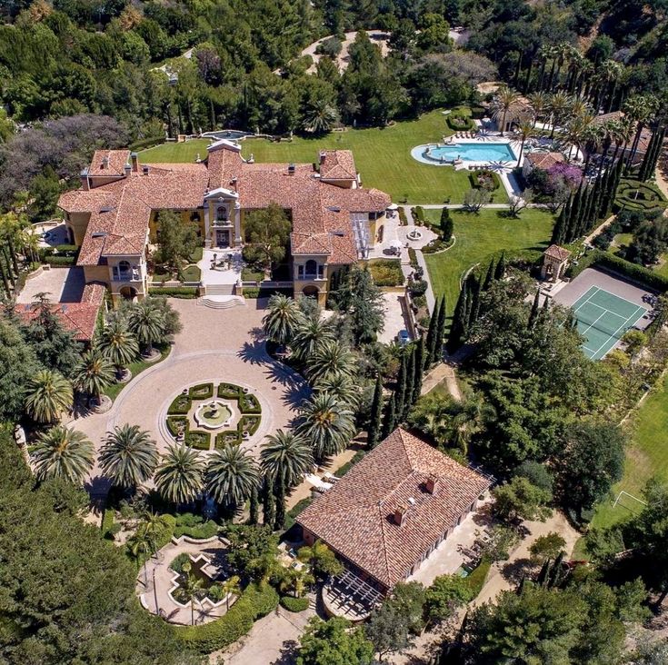 an aerial view of a large mansion surrounded by trees and bushes with a tennis court in the middle