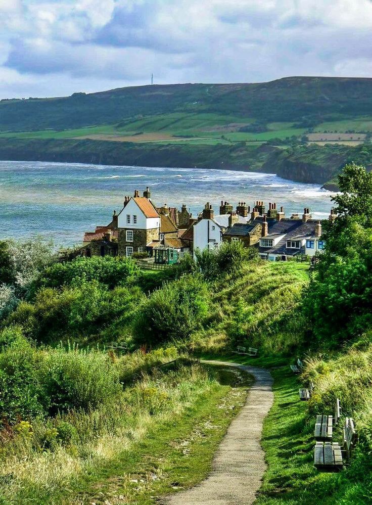 a path leading down to the beach with houses on it and water in the background