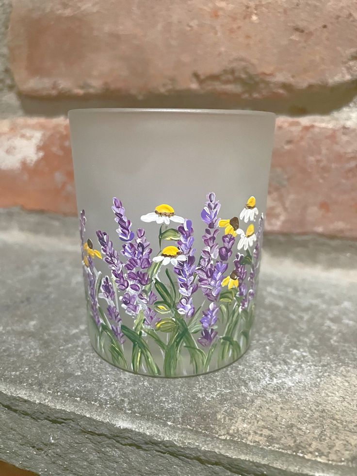 a glass vase with flowers painted on it sitting on a stone ledge next to a brick wall