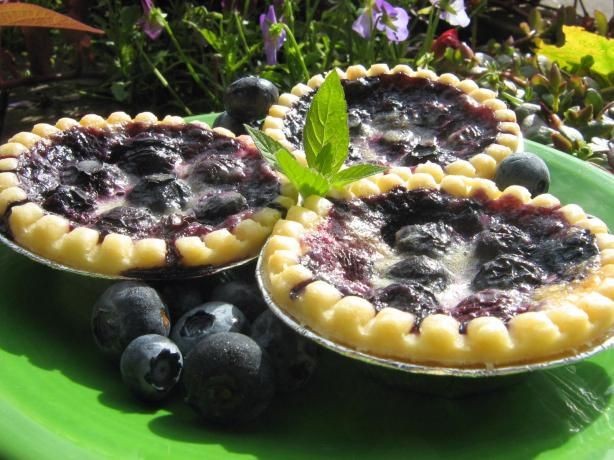 two pies with blueberries and mint sit on a green plate