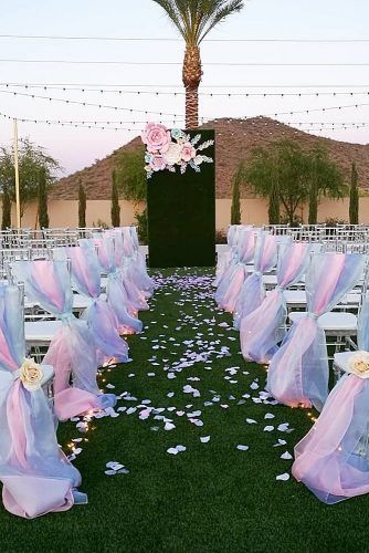 rows of chairs with pink and blue sashes are set up for an outdoor ceremony