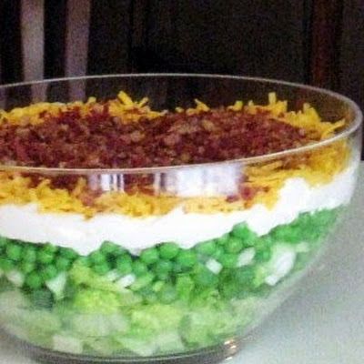 a layered salad in a glass bowl on top of a table with the words, 7 layered salad by cookingwithk net