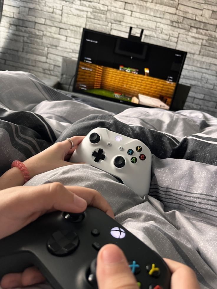 two people are playing video games together on the bed and one is holding a controller