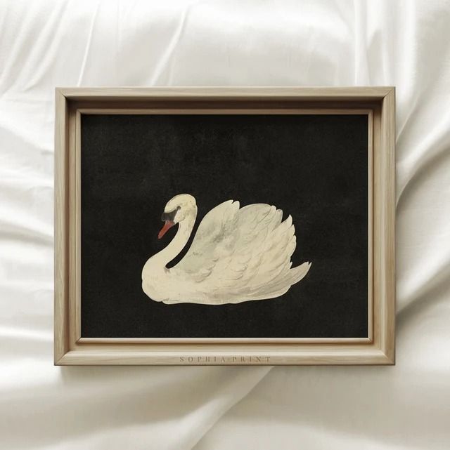 a white swan sitting on top of a bed next to a black wall mounted painting