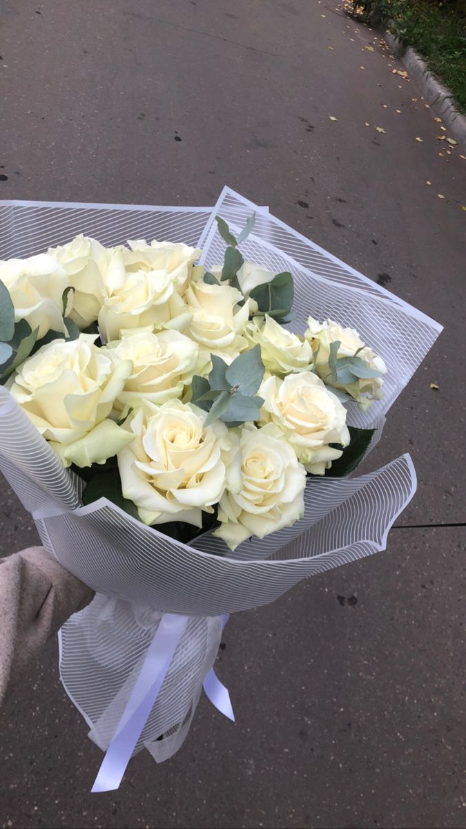 a bouquet of white roses is held by someone's hand on the side walk