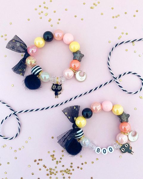 two bracelets with bows and beads on top of a pink table next to confetti