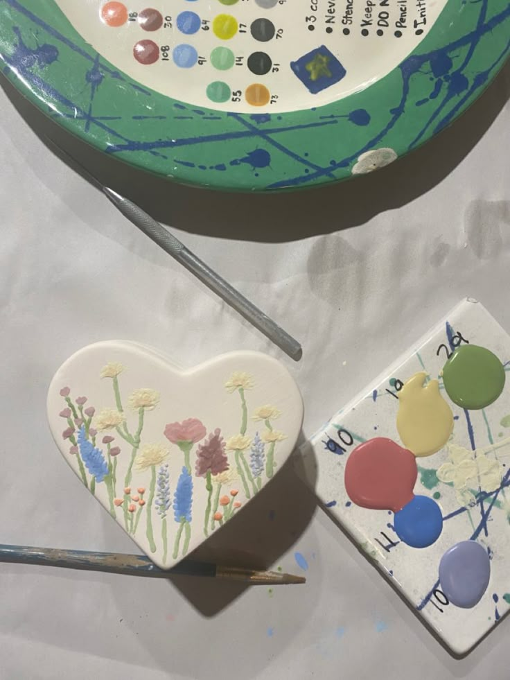 two heart shaped magnets sitting on top of a table next to paintbrushes