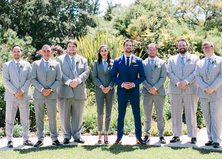 a group of men standing next to each other in front of trees and bushes with their hands behind their backs