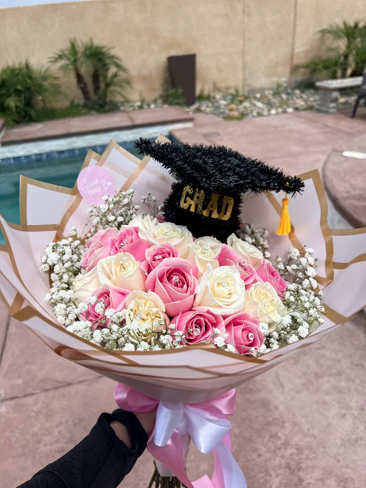 a graduation cap on top of a bouquet of flowers in front of a swimming pool