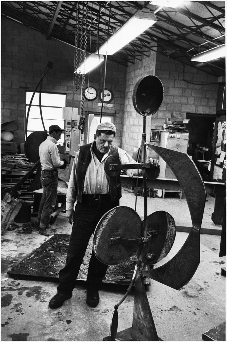 a man standing next to a large metal object in a room with other men working on it