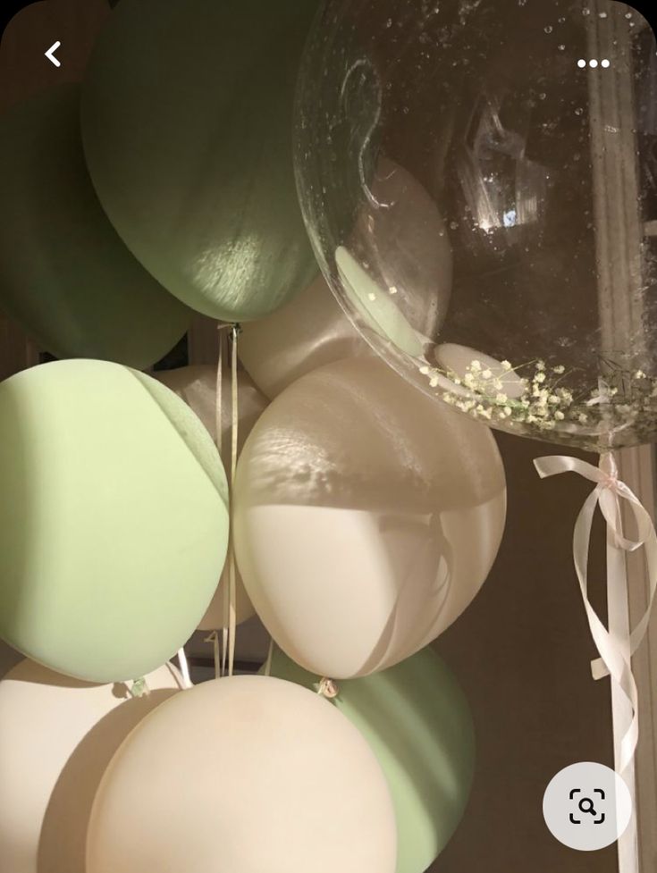 some balloons are hanging from the ceiling with white and green ribbons on them in front of a mirror