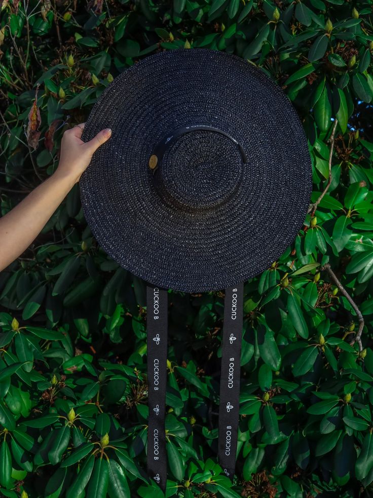 This handwoven wheat straw boater hat is handmade by Portuguese artisans, using traditional millinery techniques. Its round shape, flat cap, and wide brim makes it the perfect accessory to wear centered or at an angle on the head. It features a thick black gross-grain ribbon with the Cuckoo B logo and metal bee, intended to be worn knotted under the chin. It is the perfect accessory for a special daytime event, or even for a day at the beach or countryside. Material: Wheat straw, gross-grain rib Handwoven Adjustable Boater Hat With Flat Brim, Adjustable Handwoven Boater Hat With Flat Brim, Kentucky Derby Woven Boater Hat With Flat Brim, Black Woven Panama Hat With Flat Brim, Black Woven Panama Hat With Short Brim, Black Woven Flat Brim Panama Hat, Handmade Black Straw Hat For Beach, Black Handwoven Hat With Curved Brim, Black Handwoven Brimmed Hat