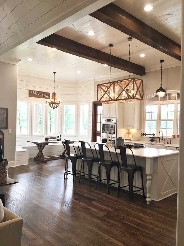 a large open concept kitchen and living room with wood flooring, white walls and beams