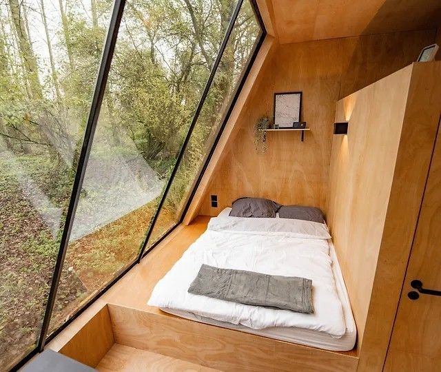 there is a small bed in the corner of this room that looks out onto the woods