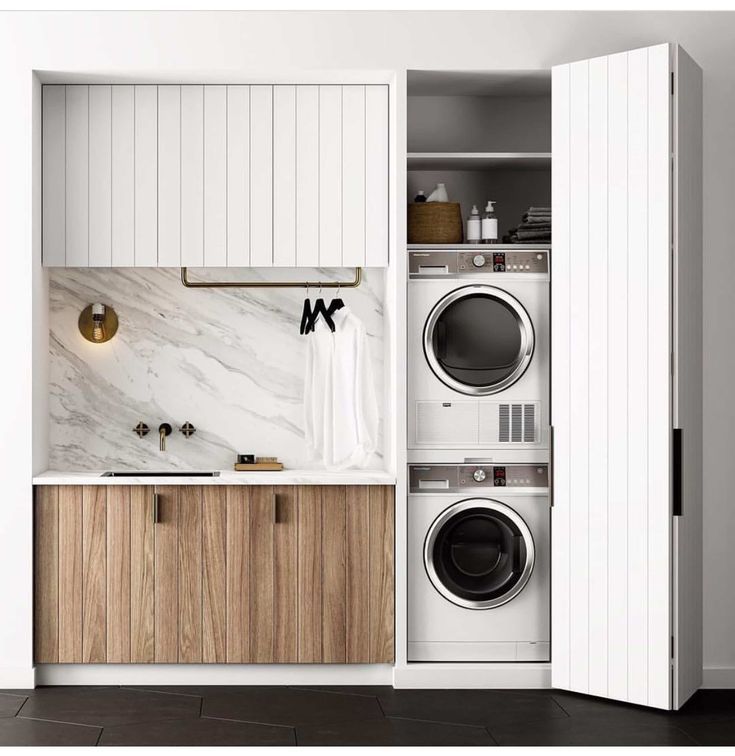 a washer and dryer in a small space with white walls, wood cabinet doors, and black tile flooring