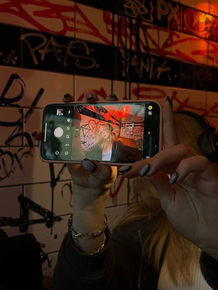 a woman taking a selfie with her cell phone in front of graffiti covered wall