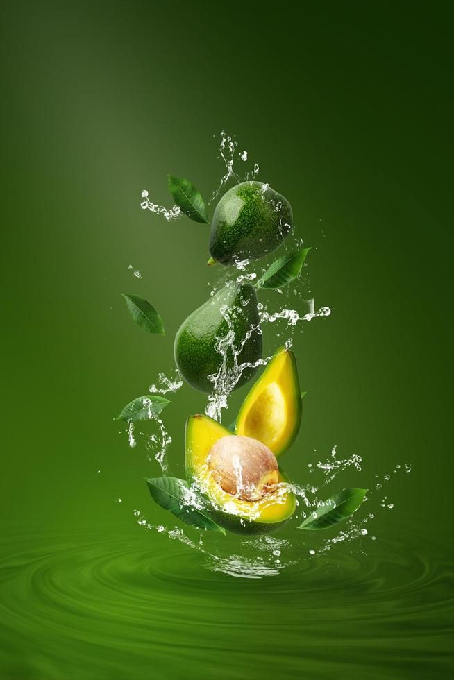 an avocado splashing into the water with its green leaves and other fruits