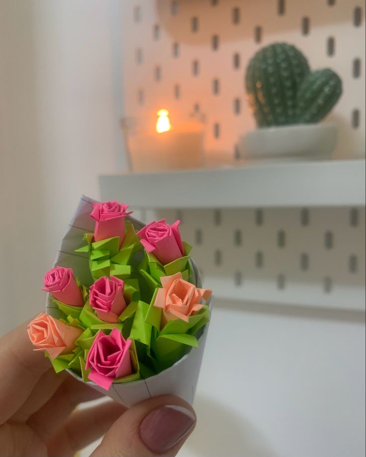 a hand holding a small bouquet of pink and green paper roses with a cactus in the background