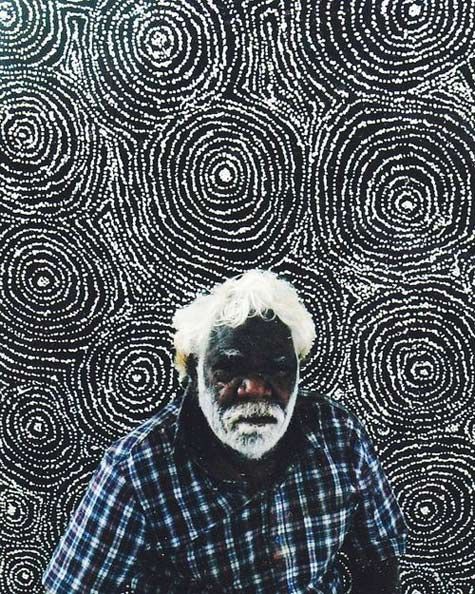 an old man standing in front of a black and white wall with circles on it