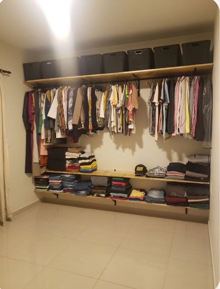 an organized closet with clothes hanging on the wall, and several bins full of shirts