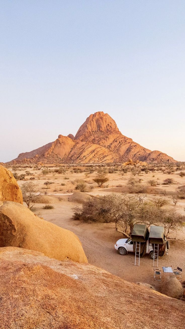 a car is parked in the desert with mountains in the background and a tent set up on top