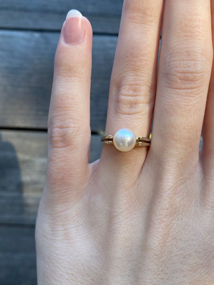 a woman's hand with a pearl ring on top of her finger, against a wooden background