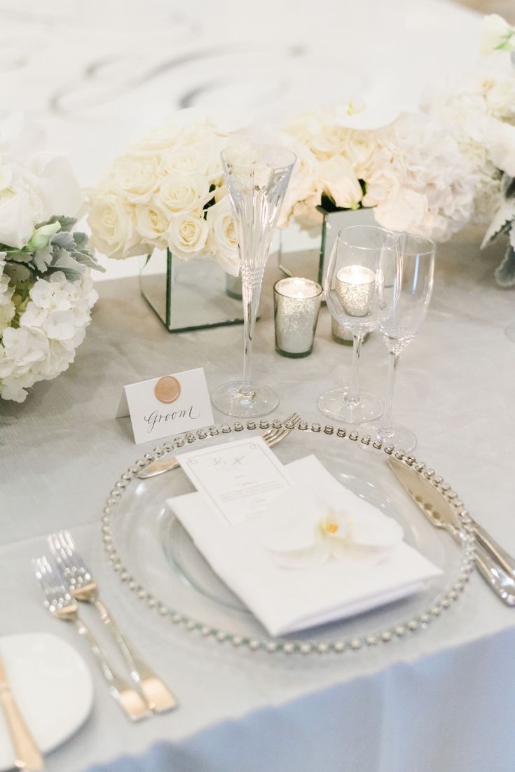 the table is set with white flowers and silverware