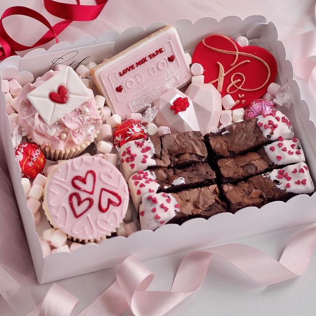 valentine's day treats in a box with pink ribbon on the table next to it