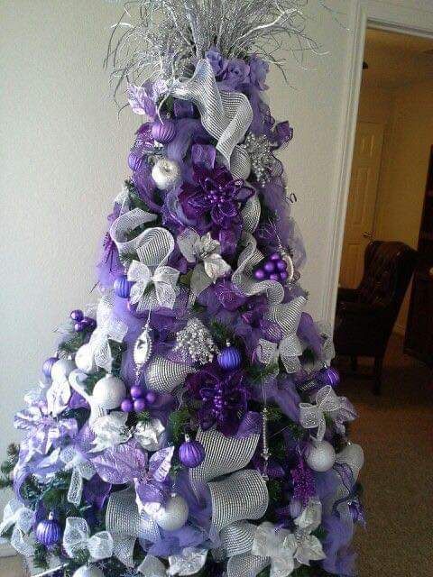 a purple and silver christmas tree is decorated with ribbons, ornaments, and bowes