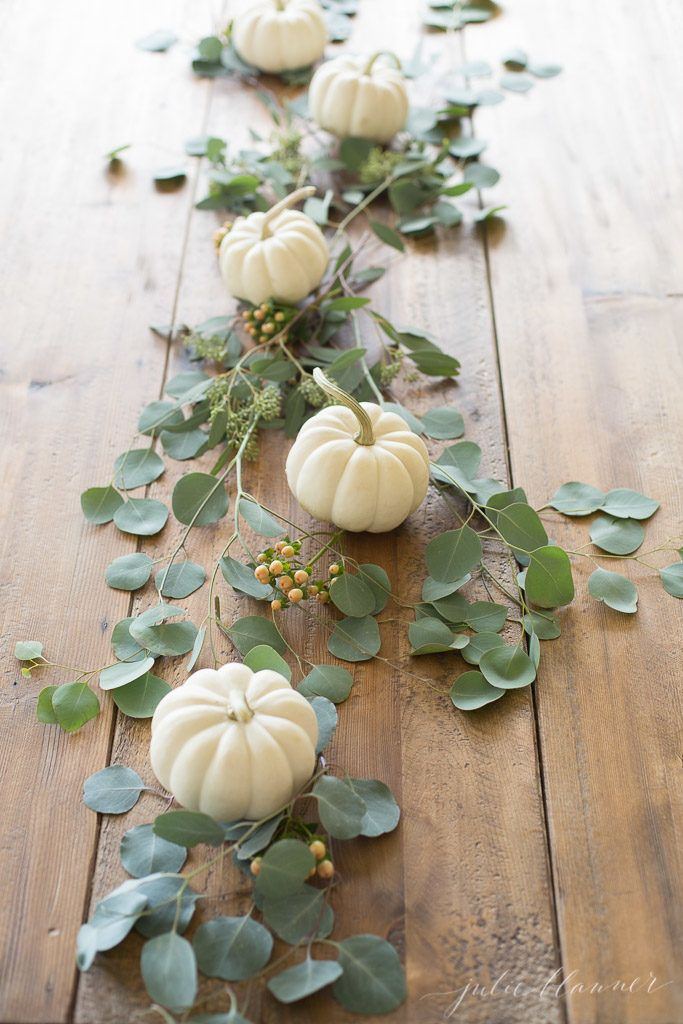 pumpkins and greenery are arranged on a wooden table