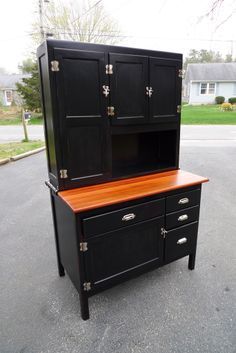 a black cabinet sitting on top of a parking lot next to a street with houses in the background