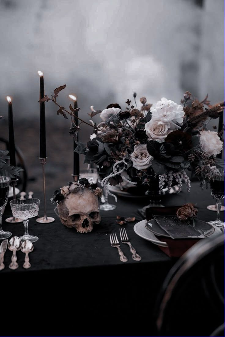 the table is set with black and white flowers, candles, silverware and skulls