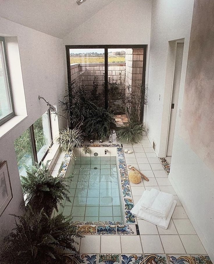 an indoor swimming pool with tiled flooring and plants in the corner next to it