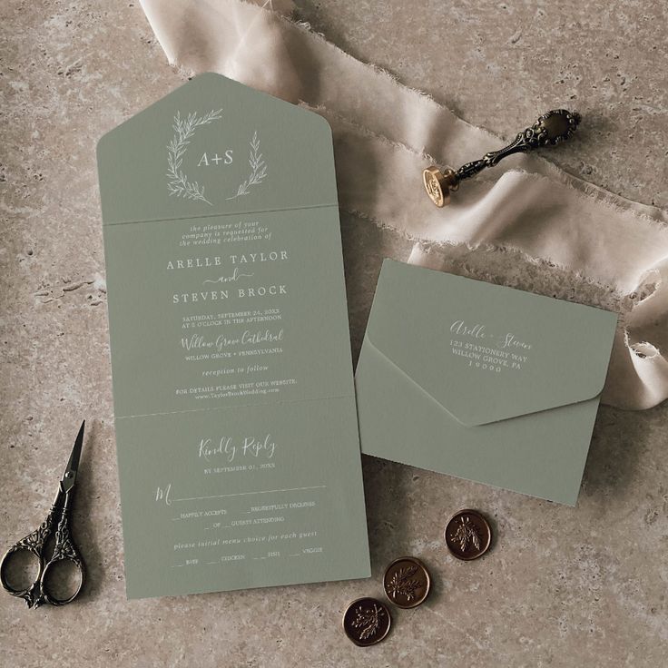 the wedding stationery is laid out on top of some fabric and two pairs of scissors