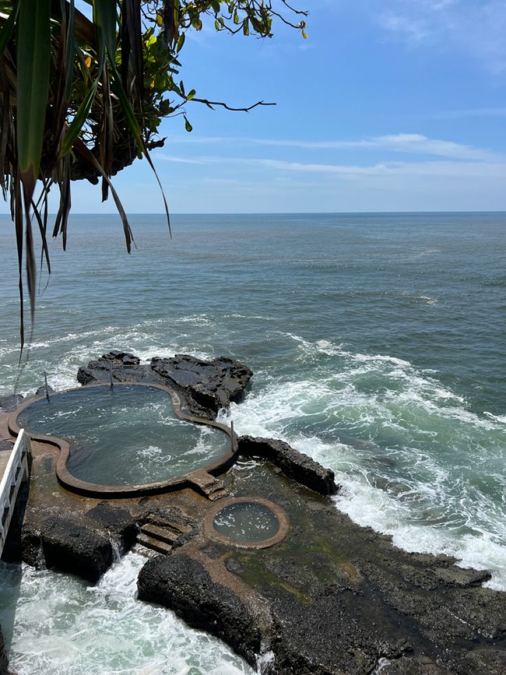 an outdoor hot tub sitting on top of a cliff next to the ocean