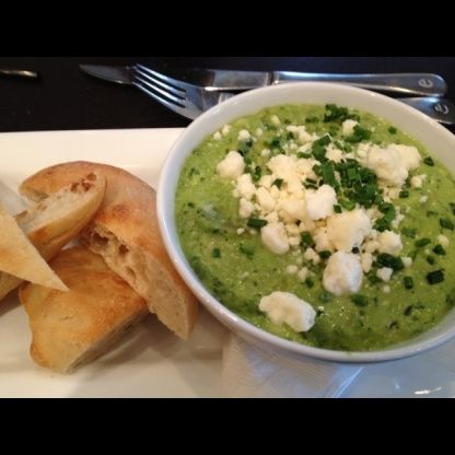 a white plate topped with bread and a bowl filled with green soup next to pita chips