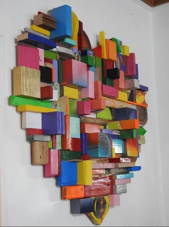 a sculpture made out of different colored objects on a white wall next to a chair